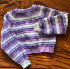 a purple and white sweater sitting on top of a bed