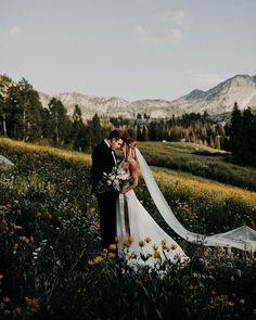 a bride and groom standing in the middle of a field with mountains in the background