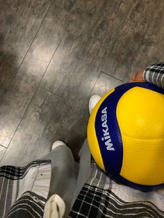 a yellow and blue ball sitting on top of a person's legs in front of a wooden floor