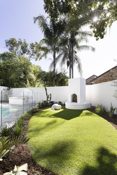 a white fenced in backyard area with grass and plants on the lawn, surrounded by palm trees