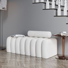 a white couch sitting in front of a stair case next to a table and chair