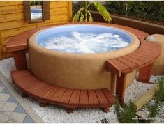 a large hot tub sitting next to a wooden bench in a backyard with gravel and plants