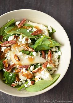 a white bowl filled with spinach, pears and feta cheese topped with pecans