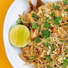 a white bowl filled with noodles, meat and veggies next to a lime wedge