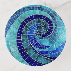 a circular blue and white mosaic tile design on a marble surface, with an abstract spiral pattern in the center