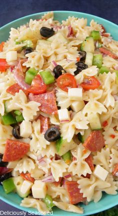 pasta salad with olives, tomatoes, and peppers in a blue bowl on a green plate