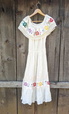 Absolutely gorgeous cream cotton Mexican sun dress, 1970s vintage. Features an off-white crinkle cotton with a subtly textured weave and slight transparency, flattering 'cold-shoulder' neckline with large ruffle, beautiful multi-colored floral embroidery along the neck ruffle and hemline, comfortable elastic 'natural' waist, full loose calf-length skirt, matching ribbon and woven lace detailing, and lots of elegant bohemian glamour... Would be perfect as a statement wedding gown for a tropical c Mexican Sun, Bohemian Glamour, White Mexican, Dress Boho Wedding, Elegant Bohemian, Crinkle Cotton, Calf Length Skirts, Peasant Dress, Lace Ribbon