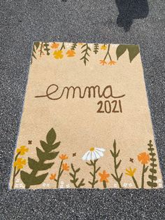 a welcome mat with flowers and leaves on the ground in front of a person's shadow