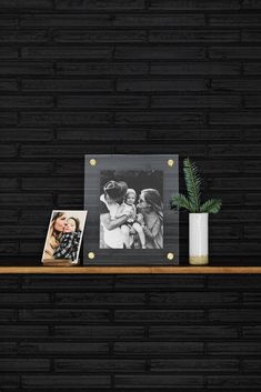 a shelf with two photos and a plant on it, next to a black wall