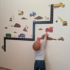 a young child reaching up to paint a wall with construction trucks and cars on it