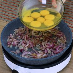 someone is adding eggs to onions in a frying pan