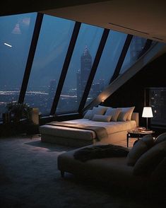 a large bed sitting in the middle of a bedroom next to a window with city lights on it