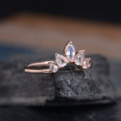 an engagement ring with three pear shaped diamonds on top of it, sitting on a rock