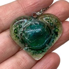 a hand holding a green heart shaped glass pendant