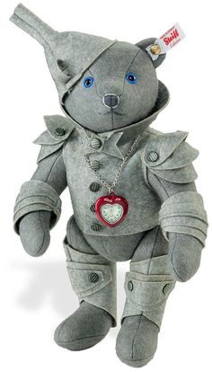 a gray teddy bear with blue eyes wearing a jacket and heart charm on it's chest