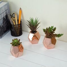 three copper geometric planters with succulents in them on a white table