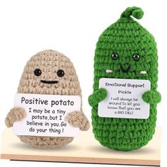 two crocheted stuffed toys sitting next to each other on a wooden shelf, one holding a sign that says positive potato and the other has an emo