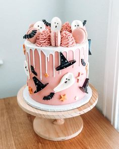 a pink halloween cake with white icing and spooky decorations on top, sitting on a wooden stand