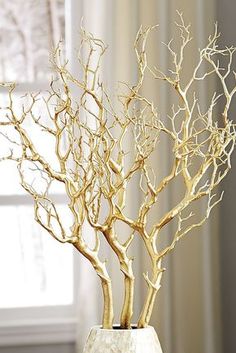 a gold tree in a white vase on a table next to a window with curtains