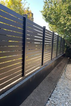 a black fence is next to some gravel and trees