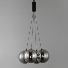 three chrome balls hanging from a black metal chandelier in a room with grey walls