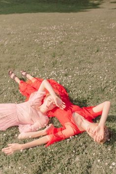 two women laying in the grass with their arms around each other and one woman wearing a red dress