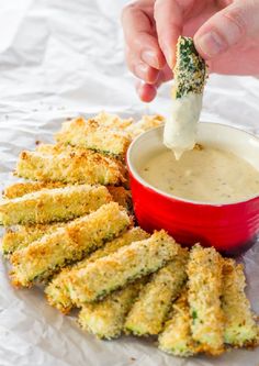 someone dipping something into a red bowl filled with dip and fried zucchini sticks