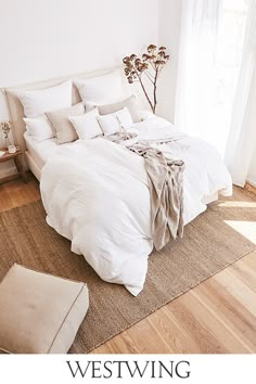 a bed with white linens and pillows in a bedroom next to a large window