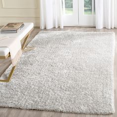 a living room with a white rug on the floor next to a window and a bench