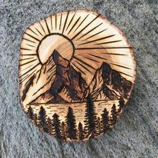 a wooden plaque with mountains and trees on it