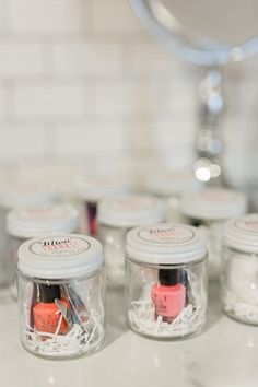 four jars with nail polish in them sitting on a counter top next to a mirror