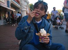 a young man eating an ice cream sundae on the sidewalk in front of shops