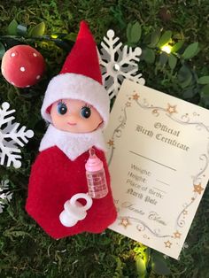 an elf doll with a birth certificate next to christmas decorations