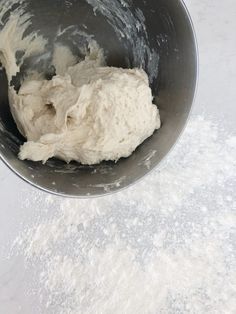 a metal bowl filled with dough on top of a white counter next to a pile of flour