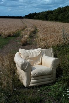 an old chair sitting in the middle of a field with no one around it,