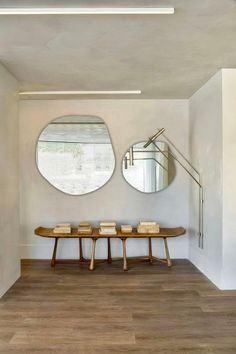 two circular mirrors are on the wall above a bench in a room with wood flooring