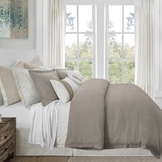 a bedroom with white walls and beige linens on the bed, along with two windows