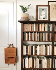 a bookshelf filled with lots of books next to a white door and framed pictures on the wall