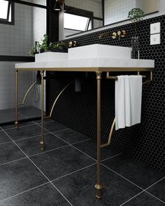 a black and white tiled bathroom with two sinks, gold fixtures and towels on the rack