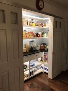 an open pantry door with food and drinks on the shelves, in front of a clock