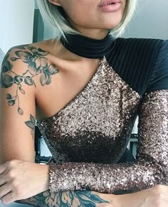 a woman with tattoos on her arm wearing a black and gold dress in front of a mirror