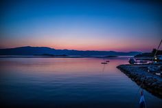 a boat is sitting in the water at dusk with mountains in the backgroud