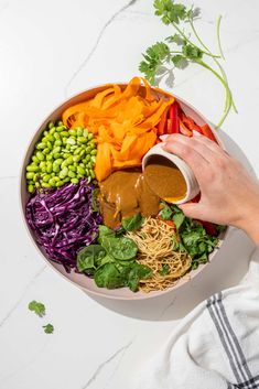 a person pouring dressing into a bowl filled with veggies and pasta salad ingredients