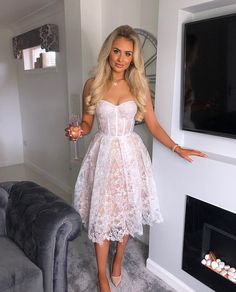 a woman in a white dress holding a wine glass and standing next to a couch