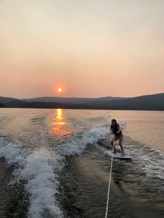 a person on a surfboard riding in the water at sunset with mountains in the background