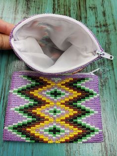 a hand holding a beaded pouch on top of a wooden table