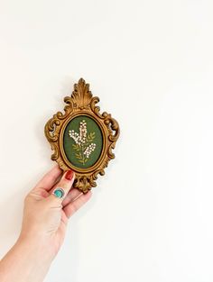 a person holding up a small gold frame with flowers on it