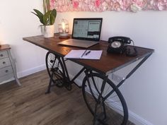 a laptop computer sitting on top of a wooden desk next to a flower covered wall