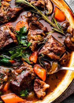 beef stew with carrots, mushrooms and parsley in a skillet on top of a table