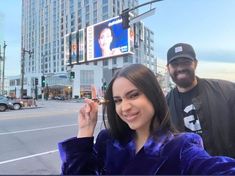 a man and woman taking a selfie in front of a city street with billboards